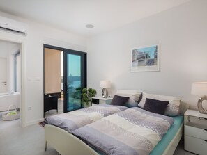 Ein modernes Schlafzimmer mit Bett, Nachttischen, einem Fenster mit Aussicht und einer Tür, die auf einen Balkon führt.
