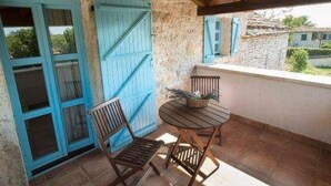 Un patio couvert avec un mur en pierre, une table en bois, deux chaises et une porte bleue.