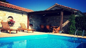 Une piscine d’un bleu éclatant, avec des chaises longues en bois et un mur en pierre.