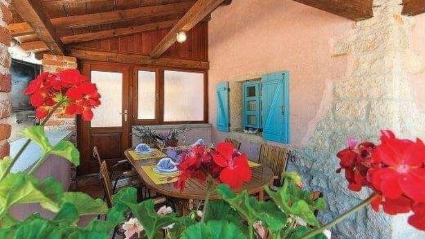 Un intérieur rustique avec un plafond en bois, une table à manger dressée avec des assiettes et des couverts, et une porte dotée de volets bleus.