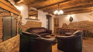 Un intérieur rustique avec des poutres en bois, des canapés en cuir, une cheminée en pierre et un coin repas.