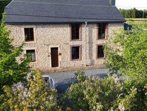 Ein Gebäude aus Stein mit mehreren Fenstern und einer Tür, umgeben von viel Grün.