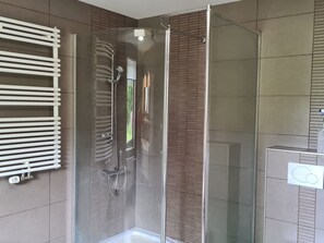 Ein modernes Badezimmer mit Duschkabine aus Glas, einem weißen Handtuchhalter und einer sichtbaren Duschsteuerung.