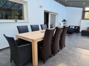 Ein Essbereich mit Holztisch und schwarzen Stühlen, eine Glastür zum Balkon und eine Couch im Hintergrund.