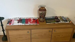 Ein Holzschrank mit Zeitschriften und einer Vase darauf.