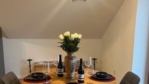 Ein Essbereich mit einem runden Tisch, vier Stühlen, einer Blumenvase, Weingläsern und Flaschen.