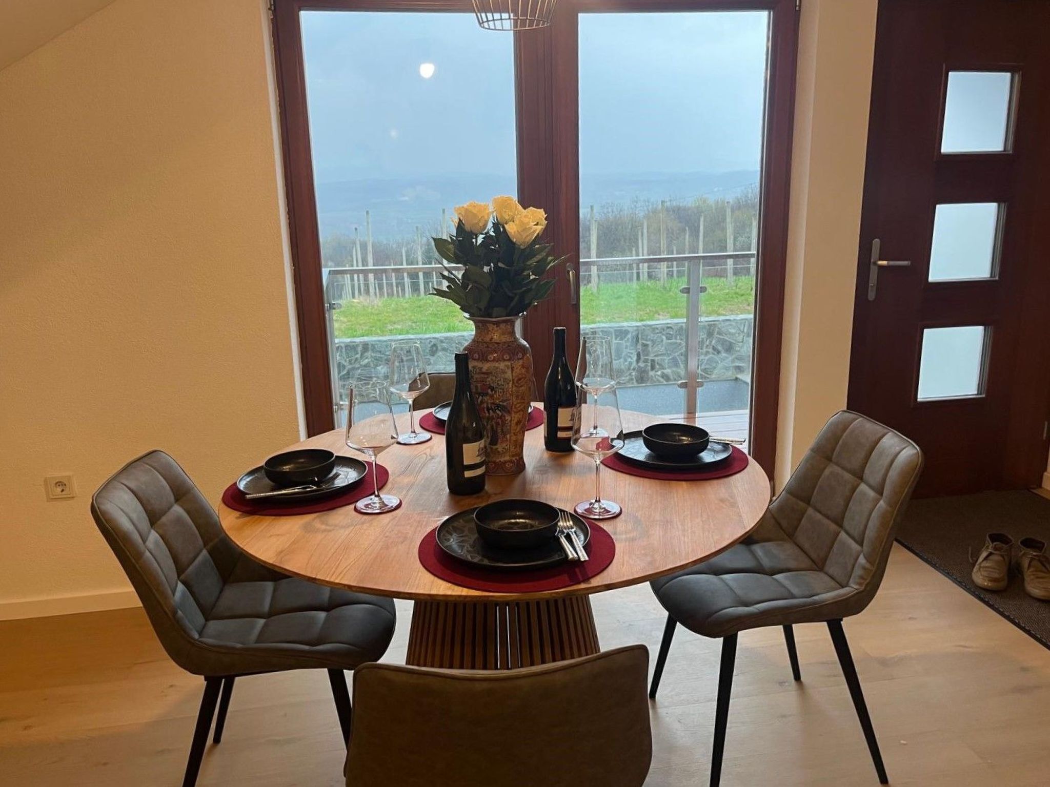 A dining area with a round table, four chairs, a vase with flowers, wine glasses, and a bottle.