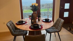 Ein Essbereich mit einem runden Tisch, vier Stühlen, einer Blumenvase, Weingläsern und einer Weinflasche.