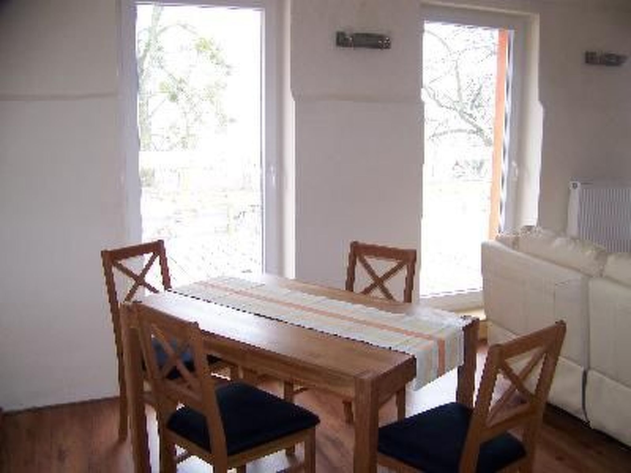 A dining area with a wooden table and chairs, a white sofa, and a window with a view of trees.