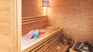 Een houten sauna met banken, een wandlamp en een emmer stenen.