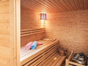 Una sauna de madera con bancos, una luz fijada en la pared y un cubo de piedras.