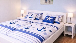 Een bed met nautische beddengoed, twee nachtkastjes met lampen, en een schilderij aan de muur.