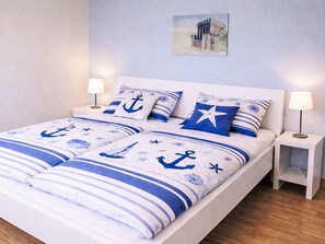 A bed with nautical-themed bedding, two bedside tables with lamps, and a painting on the wall. - in Pruchten mit Sauna und Kamin by Interhome (Bodstedt)