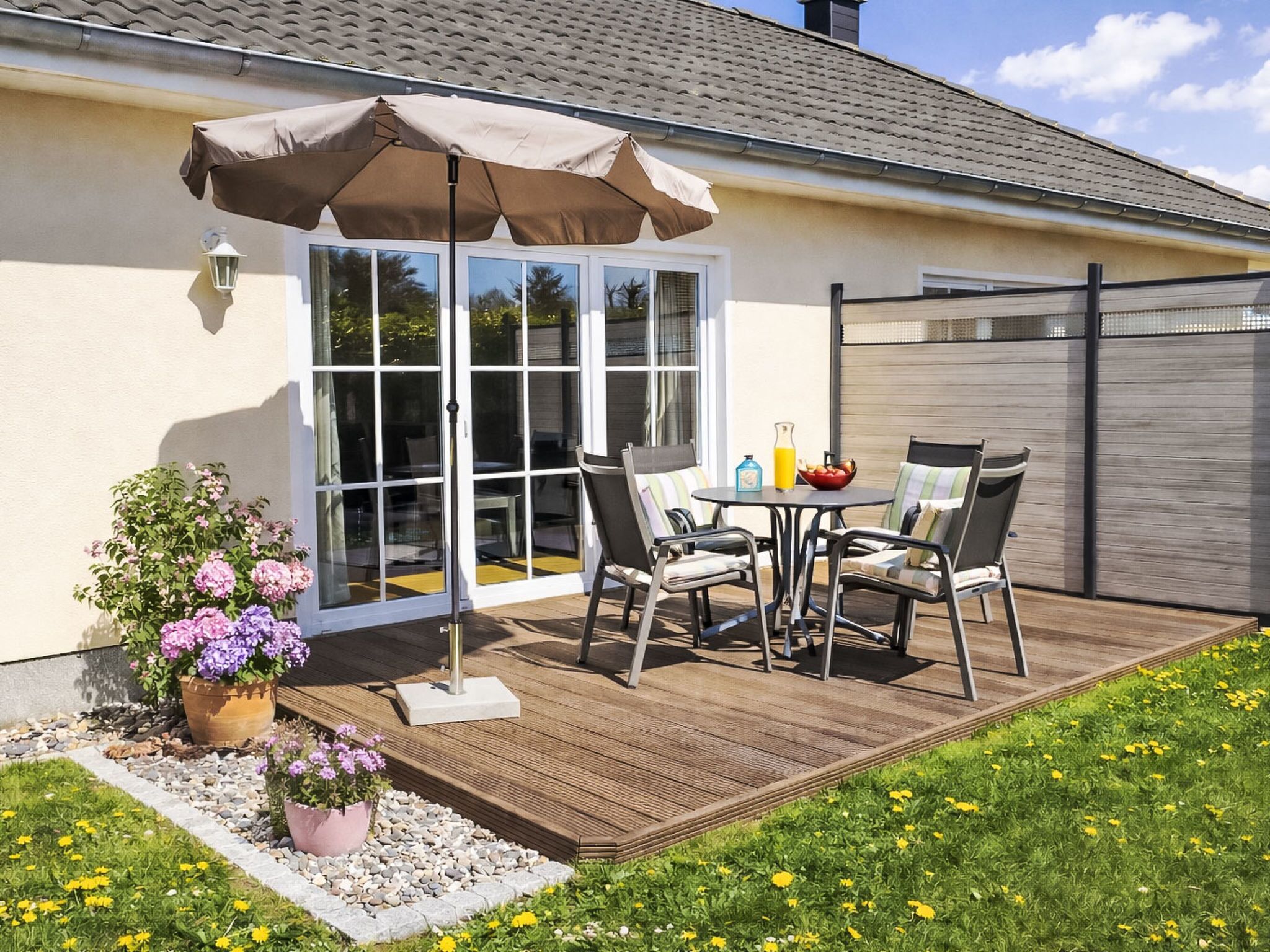 Eine Terrasse mit Tisch, Stühlen und einem Blumentopf, sowie eine Glastür, die sich öffnen lässt.