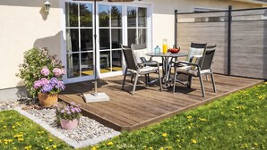 Een terras met een tafel, stoelen, een plant in pot en een schuifdeur.