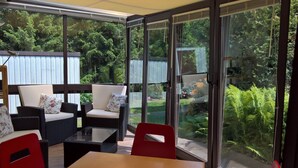 A sunroom with large sliding glass doors, wicker furniture, and a table. - in Maxen mit Privatem Pool by Interhome (Maxen)