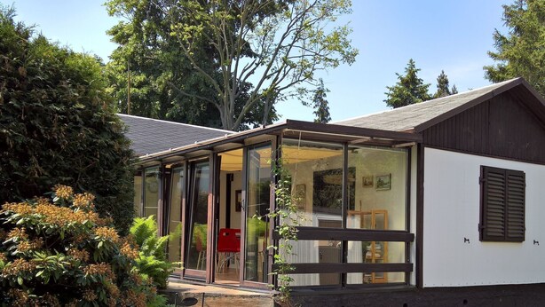 A modern house with a glass door entrance, a small porch, and a garden area with plants and a red chair. - in Maxen mit Privatem Pool by Interhome (Maxen)
