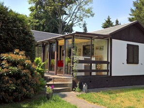 A modern house with a glass door entrance, a small porch, and a garden area with plants and a red chair. - in Maxen mit Privatem Pool by Interhome (Maxen)