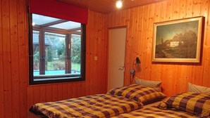 A room with wooden walls, a bed with striped bedding, a window with a view of greenery, and a painting on the wall. - in Maxen mit Privatem Pool by Interhome (Maxen)