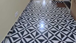 Un couloir doté d’un sol à motifs géométriques, une porte au fond et une petite fenêtre à carreaux.
