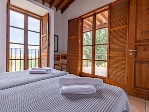 Une chambre avec deux lits, des volets en bois et un balcon.