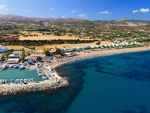 Vista aérea de uma área costeira com um porto de iates, praia e edifícios residenciais.
