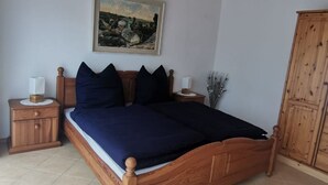 Ein Schlafzimmer mit einem hölzernen Bett, einem Nachttisch, einer Lampe, einem Bild an der Wand und einem Kleiderschrank.