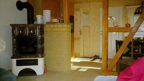 Une cuisine équipée d’un poêle à bois, d’un plan de travail carrelé et d’un escalier en bois menant à une autre pièce.