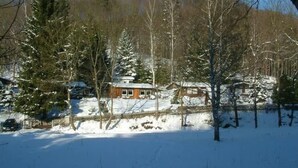 Une cabane entourée d’arbres couverts de neige et d’une clôture en bois.