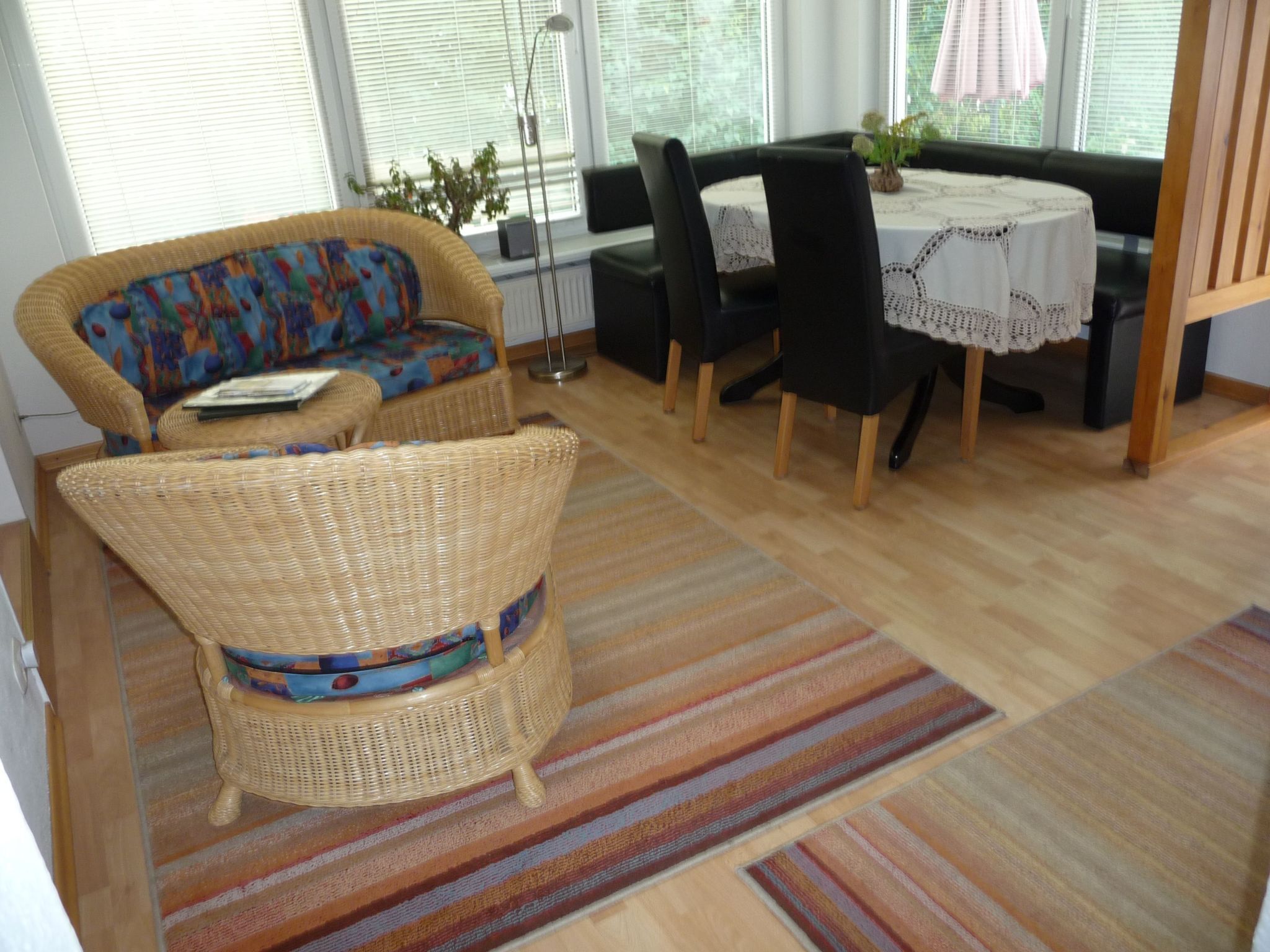 A room with a wicker sofa, a dining table with chairs, and a striped rug.