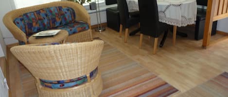 Una habitación con sofá de mimbre, una mesa de comedor con sillas y un tapete a rayas.