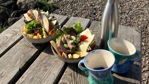 Ein Picknick auf einem Holztisch an einem felsigen Strand mit Blick auf das Meer.