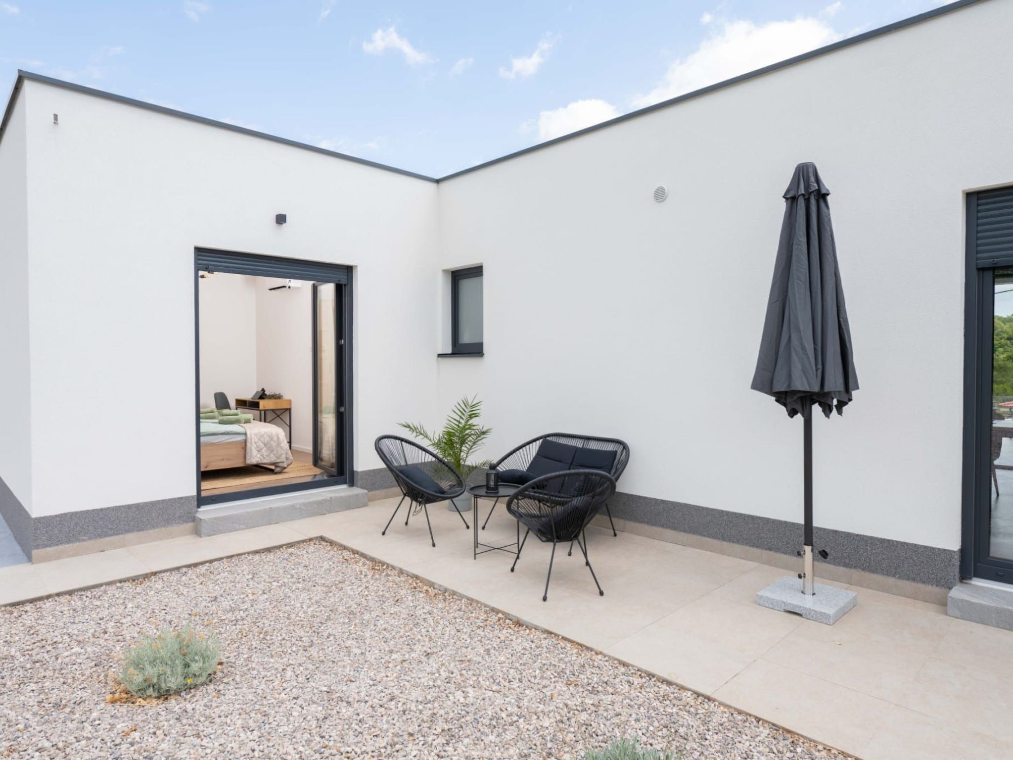 A modern outdoor patio area with a seating arrangement, a covered umbrella, and a door leading to a bedroom.