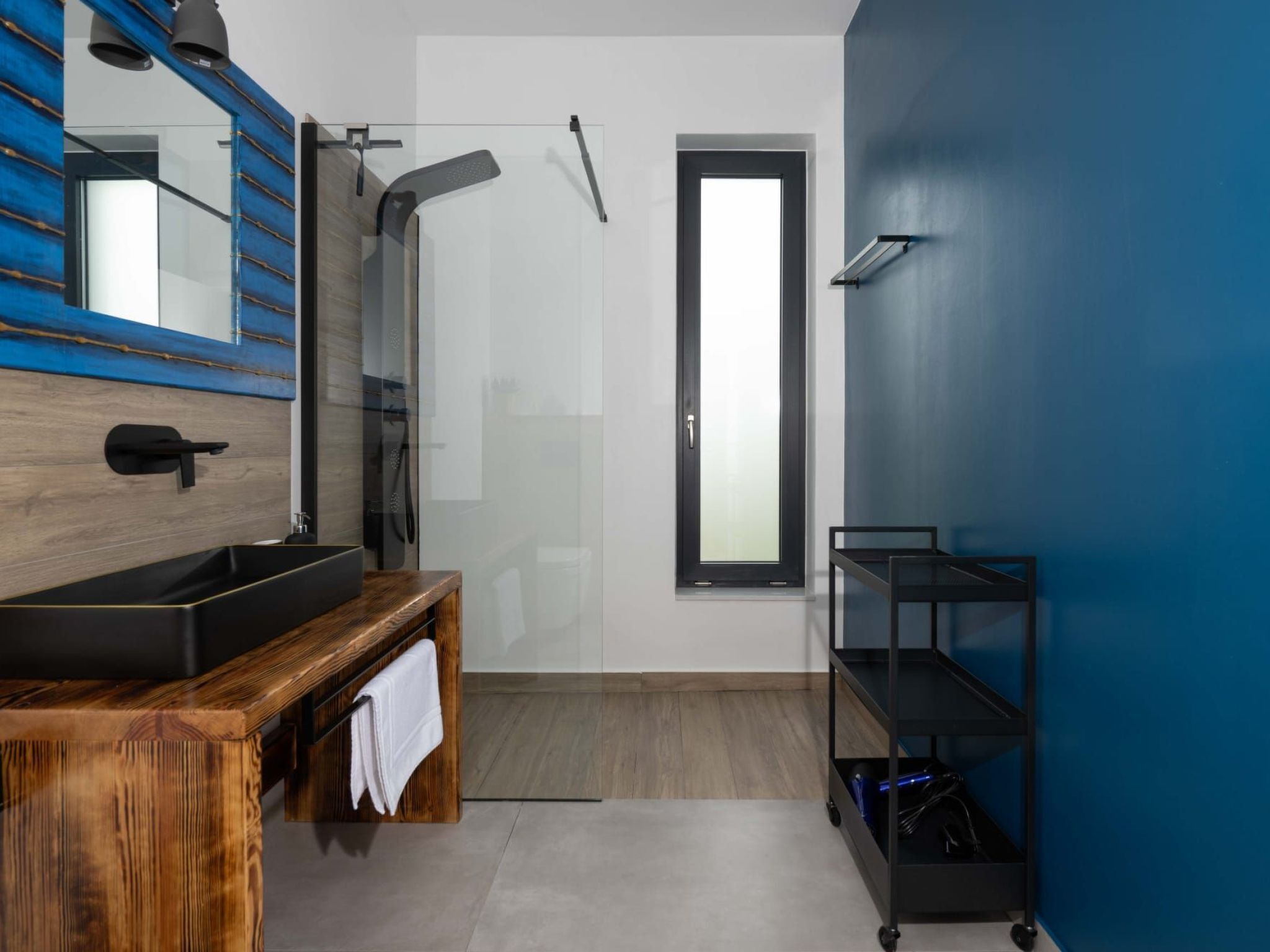 Une salle de bain moderne avec un meuble-lavabo en bois, une cabine de douche en verre et un mur d’accent bleu.
