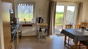 Une cuisine compacte avec une fenêtre, un coin repas comprenant une table et des chaises, et une vue sur une terrasse en bois à l’extérieur.