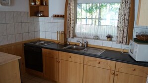 Una cucina con mobili in legno, lavastoviglie, fornello, lavandino e una finestra con tende.
