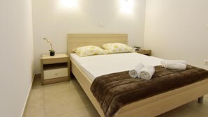 A modern bedroom with a wooden bed, two bedside tables, a nightstand, a small potted plant, and two wall-mounted lights. - Apartment NOA 4 by Interhome (Poreč/Tar)