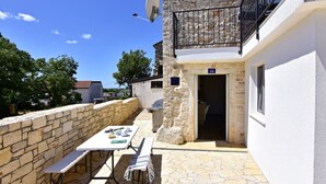 Eine Terrasse im Freien mit Steinmauern, einem Tisch und Bänken, einer Satellitenschüssel und einem Balkon mit schwarzem Geländer.