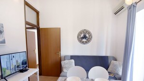 Un comedor con una mesa dispuesta para cuatro, un reloj en la pared y un televisor sobre un mueble.
