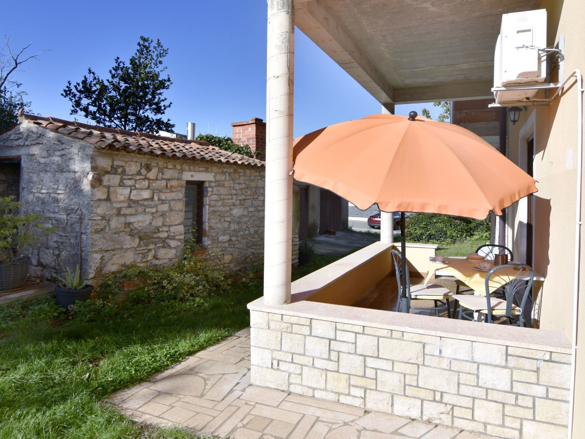 Ein Steinhaus mit einem Ziegeldach, einer Terrasse mit Tisch und Stühlen sowie einem großen orangefarbenen Sonnenschirm.