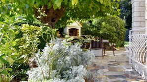 Un patio de piedra con un banco de metal blanco y una pequeña construcción de madera al fondo.