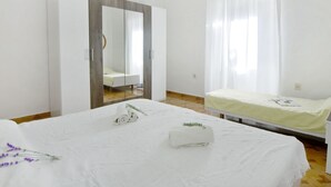 Un dormitorio moderno con una cama grande, otra más pequeña, un armario y un baño visible a través de una puerta de cristal.