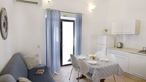 Un espacio habitable compacto con zona de comedor, kitchenette y un sofá con una revista.