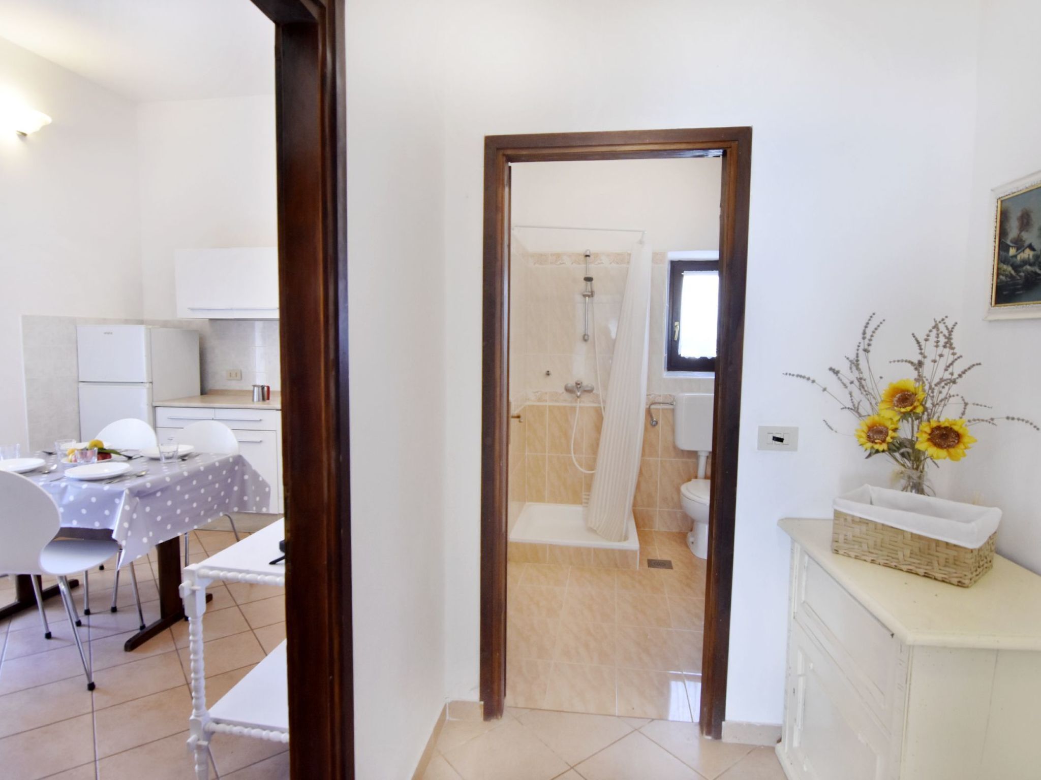 Una habitación con una mesa de comedor preparada para dos personas, una zona de cocina y un baño con ducha e inodoro a la vista a través de un acceso.