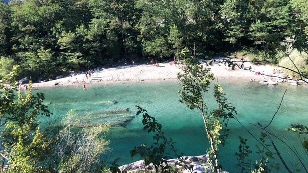 Paesaggio naturale con un lago turchese cristallino circondato da fitta vegetazione e terreno roccioso.