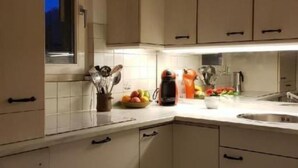 Una cucina con mobili color beige, una finestra con tenda, un fornello e un lavello.