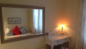Una camera da letto con un letto, un comodino con una lampada, uno specchio e una finestra con tende.