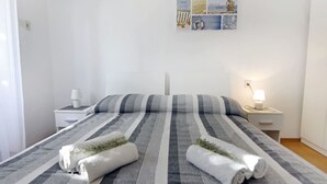 Un lit bien fait, avec une literie à rayures, deux serviettes blanches ornées de motifs végétaux, une table de chevet avec une lampe, et une œuvre d’art murale au-dessus du lit.
