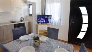 Une cuisine moderne avec des meubles blancs, une cuisinière noire et un coin repas agrémenté d’une nappe à pois, de chaises et d’un téléviseur diffusant une émission.
