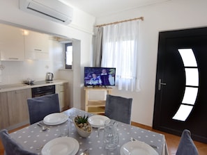 A modern kitchen with white cabinets, a black stove, and a dining area with a polka dot tablecloth, chairs, and a TV displaying a show. - Silva B4+1 by Interhome (Umag/Savudrija)